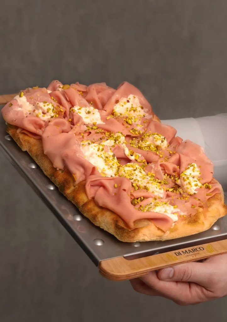 Pinsa con mortadella, stracciatella e granella di pistacchio servita su una pala